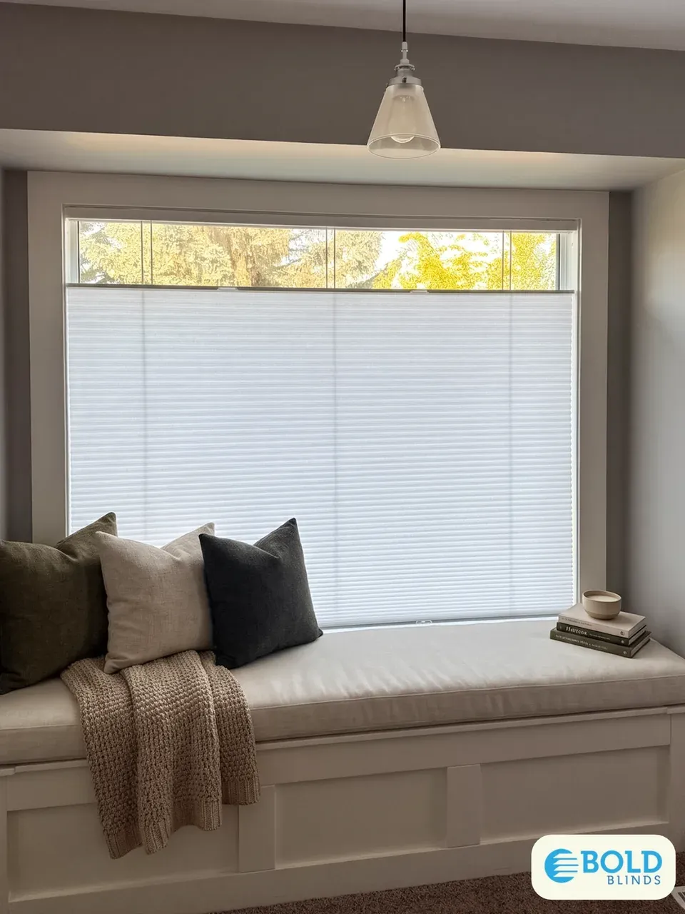 Top-down/bottom-up honeycomb shade on a window seat, lowered from the top to let in daylight