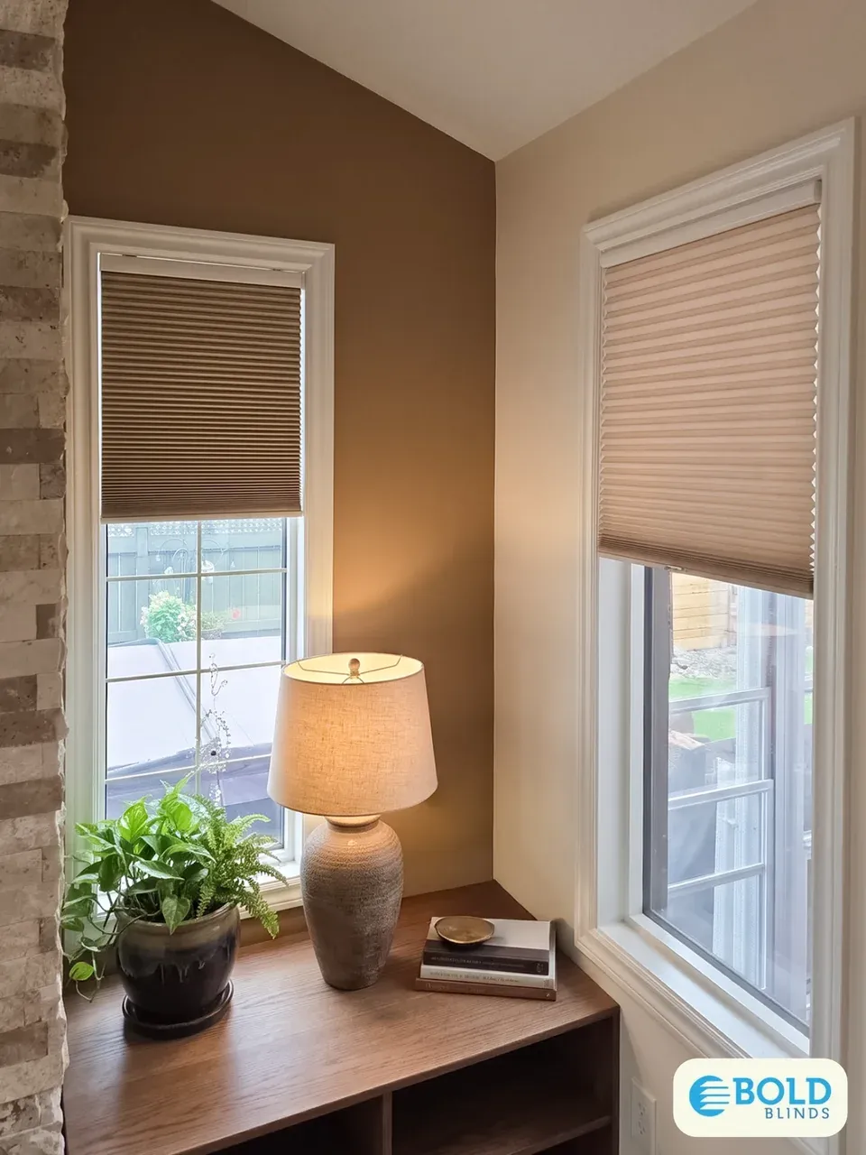 Honeycomb shades partly raised on two tall corner windows beside a wooden console